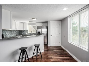Modern kitchen features white cabinets, stainless steel appliances, breakfast bar, and hardwood floors at 5250 S Huron Way # 13-312, Littleton, CO 80120