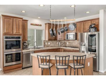 Well-lit kitchen features wood cabinetry, tiled countertops and backsplash, stainless appliances, and a central island with seating at 1335 Galactic Pl, Castle Rock, CO 80108