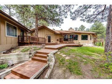 Inviting home exterior featuring a wooden deck, manicured lawn, and mature trees, creating a serene outdoor space at 8788 E Tanglewood Rd, Franktown, CO 80116
