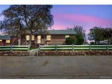 Charming single-story brick home with a white picket fence and stone retaining wall at 6895 E 74Th Ave, Commerce City, CO 80022