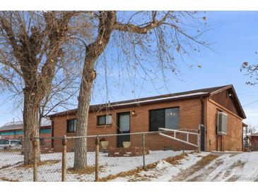 Brick ranch home with snow-covered yard and trees at 7600 Monaco St, Commerce City, CO 80022