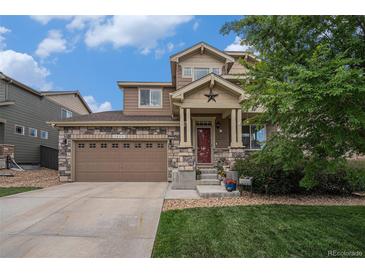 Charming two-story home featuring a stone facade, covered porch with star detail, and attached two-car garage at 7877 E 139Th Pl, Brighton, CO 80602