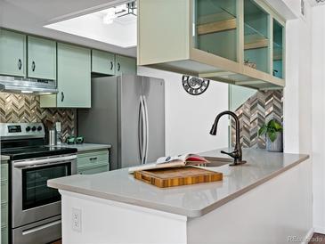 Well-lit kitchen featuring stainless steel appliances, light green cabinets, and stylish backsplash and countertop at 7770 W 87Th Dr # F, Arvada, CO 80005