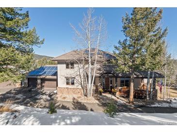 Inviting two-story home featuring a stone facade, covered porch, and a three-car garage with solar panels at 3064 Elk View Dr, Evergreen, CO 80439