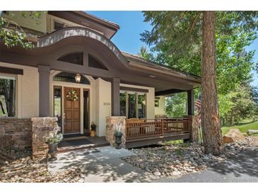 Inviting home entrance featuring a covered porch with stone accents and a charming wooden door at 3064 Elk View Dr, Evergreen, CO 80439