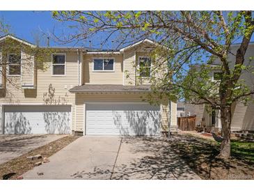 A charming townhouse with a two-car garage and light-yellow siding, with a beautiful tree and blue skies at 817 Pintail Ave, Brighton, CO 80601