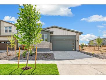 Charming home with a grey garage door, brick and hardiplank siding, and a young tree in the front yard at 9332 Bahama Ct, Commerce City, CO 80022