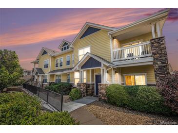 Charming yellow townhome exterior with stone accents and inviting front porch with beautiful dusk sky at 9434 Ashbury Cir # 204, Parker, CO 80134