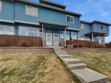 Blue townhouse exterior with a covered entrance, steps leading up, and a small front yard at 12032 Leyden St, Brighton, CO 80602