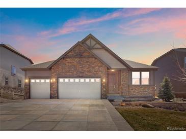 Charming exterior elevation showcases a stone facade, two-car garage, and well-manicured lawn against a colorful twilight sky at 27234 E Quarto Ave, Aurora, CO 80016