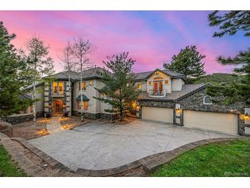 Elegant home with a three car garage, stone accents, mature trees, and a beautifully lit driveway at dusk at 22554 Treetop Ln, Golden, CO 80401