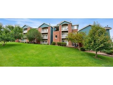 Well-maintained condo building featuring lush green lawn and mature trees at 2705 S Danube Way # 103, Aurora, CO 80013