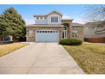 Charming two-story home with brick and light blue accents, a well-manicured lawn, and an attached two-car garage at 13078 Monaco Way, Thornton, CO 80602
