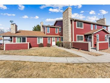 Charming townhouse with red siding, stone chimney, well-maintained lawn, and inviting curb appeal at 8424 Everett Way # E, Arvada, CO 80005
