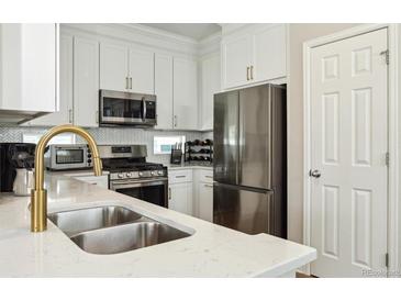 Modern kitchen with stainless steel appliances, gold faucet, white cabinets and marble countertops at 3178 Geneva Ct, Denver, CO 80238