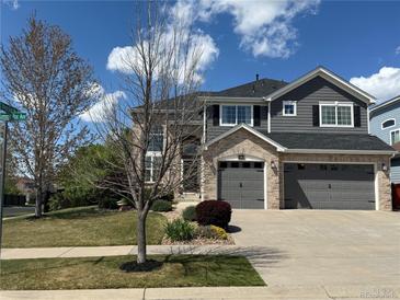 Beautiful two-story home featuring a three-car garage, manicured lawn, and a mix of stone and gray siding at 15915 E Summit Fox Ave, Parker, CO 80134