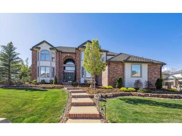 A well-manicured front yard featuring a brick home, steps leading to the front door, and mature landscaping at 9188 Buck Hill Dr, Highlands Ranch, CO 80126
