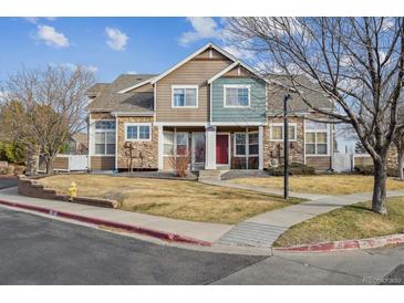 Two-story townhome featuring stone accents, a red front door, and a well-maintained front lawn at 13271 Holly St # D, Thornton, CO 80241
