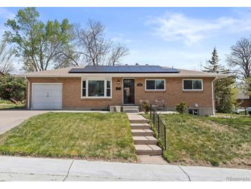 Inviting brick home with solar panels, features an attached garage, and cozy front porch seating at 4102 W Eastman Ave, Denver, CO 80236
