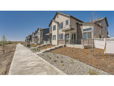 Modern townhome exteriors with light colored wood siding and brick accents along a sidewalk under a bright blue sky at 1224 S Algonquian St, Aurora, CO 80018