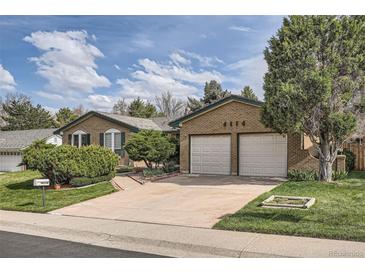 Charming brick home with a two-car garage and beautifully landscaped front yard on a sunny day at 4114 S Niagara Way, Denver, CO 80237