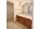 Bathroom vanity with warm wood cabinetry, a large mirror, and a glimpse into the shower/tub area at 13661 Adams St, Thornton, CO 80602
