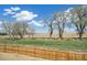 View of a large backyard with trees and a wooden fence, showing open fields and clear blue sky at 6207 E 155Th Pl, Brighton, CO 80602