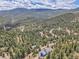 Aerial view of a blue home in the mountains surrounded by trees and winding roads at 33633 Elk Run, Evergreen, CO 80439