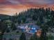 Stunning aerial view of a blue home nestled in a forest against a colorful sunset sky at 33633 Elk Run, Evergreen, CO 80439
