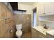 Bathroom featuring earth-toned tile and a white toilet, sink with storage, and floating black shelves at 5185 Alcott St, Denver, CO 80221