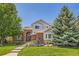 Charming two-story home featuring a brick facade, arched entryway, lush landscaping, and mature trees at 13901 Quail Ridge Dr, Broomfield, CO 80020