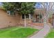 Charming brick home with a lush green lawn, mature tree, and covered porch area with seating at 3667 Hudson St, Denver, CO 80207