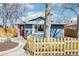 Blue single-story home featuring a red door, large window, light-colored fence, and a tree in the front yard at 214 N 10Th Ave, Brighton, CO 80601