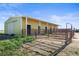A yellow barn with multiple stalls and doors, perfect for horses or livestock, sits under a sunny blue sky at 29881 E 128Th Ave, Commerce City, CO 80022