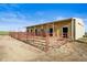 A yellow barn with multiple stalls and doors, enclosed with red pipe fencing, sits under a sunny blue sky at 29881 E 128Th Ave, Commerce City, CO 80022