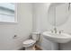 Bathroom with a pedestal sink, round mirror, white toilet, and window at 9297 Truckee Ct, Commerce City, CO 80022
