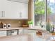 Bright kitchen with white cabinets, stainless steel dishwasher, light countertops, and a view of the backyard at 9016 W Alabama Pl, Lakewood, CO 80232