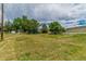 Expansive property featuring a large grassy area, mature trees, a white fence, and outbuildings under a cloudy sky at 7684 Beverly Blvd, Castle Pines, CO 80108