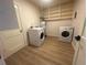 Bright laundry room with a washer, dryer, water heater, storage shelves, and wood-look vinyl floors at 1120 Tucson St, Aurora, CO 80011