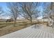 Large backyard with deck, mature trees, play structure, and white fence, perfect for outdoor enjoyment at 16021 Verbena St, Brighton, CO 80602