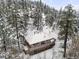 Overhead winter view showcases a home with a wraparound deck surrounded by snow-covered trees on a mountainside at 11710 Spruce Canyon Cir, Golden, CO 80403