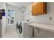 Bright laundry room with white washer and dryer, overhead shelves, and a view from the window at 16123 Quarry Hill Dr, Parker, CO 80134