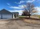 Home exterior featuring an attached garage, gravel driveway, and mature trees in a sunny neighborhood at 51 W 6Th Pl, Byers, CO 80103