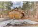 Rear-side exterior view of the home featuring a two-car garage, brick accents, and pine tree-filled landscape at 70 Long Bow Cir, Monument, CO 80132