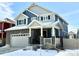 Two-story home with stone accents and a covered front porch, featuring a two-car garage, located in a snow-covered neighborhood at 1048 Larkspur Dr, Erie, CO 80516