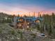 Stunning exterior shot of mountain home with a stone chimney, walkway and hot tub nestled amongst mature trees at 23 Verde Ct, Breckenridge, CO 80424