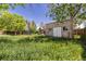 View of the spacious backyard with overgrown grass and a shed, plus a play structure and trampoline at 140 S Kendall St, Lakewood, CO 80226