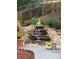 Backyard waterfall feature with decorative statues, lush plantings, and a cozy bench at 975 S Queen Way, Lakewood, CO 80226