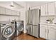 Well-lit laundry area with stainless steel washer, dryer, and refrigerator situated next to white kitchen cabinetry at 1827 Quail St # 8, Lakewood, CO 80215