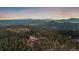 Expansive aerial view showcases the home nestled amongst mountains and lush forests during golden hour at 23007 Big Game Trl, Conifer, CO 80433